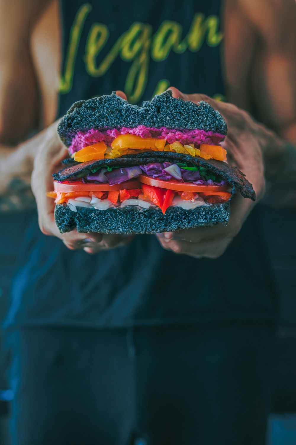 person holding meat sandwich with sliced tomatoes, onions, and grilled meat