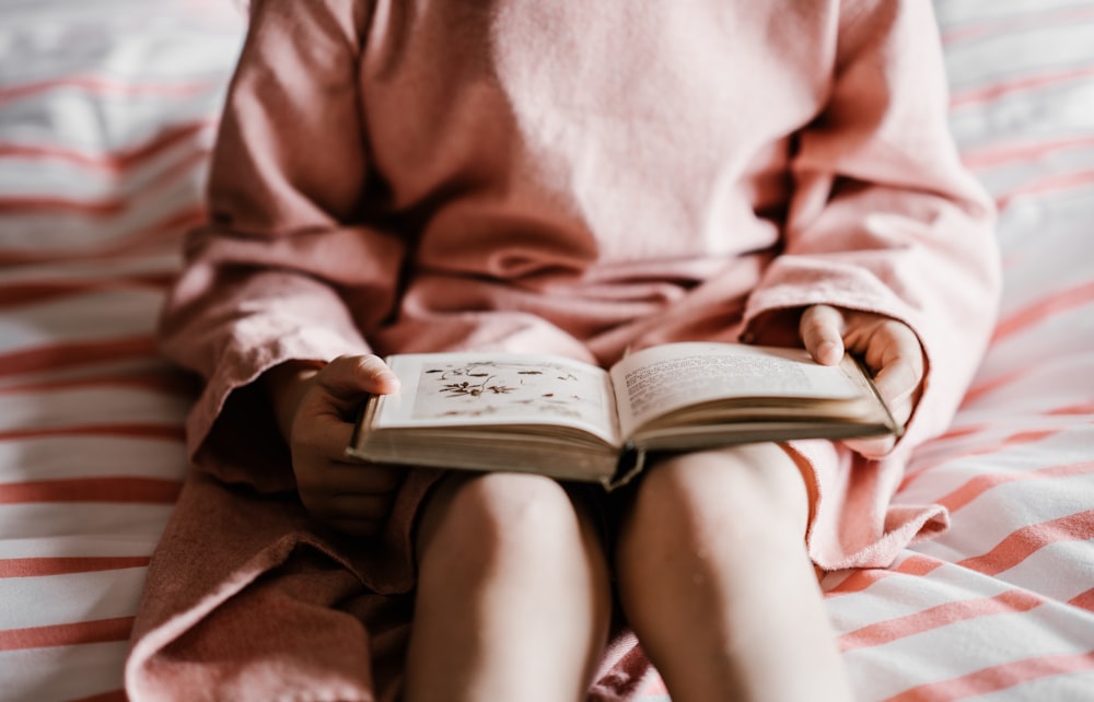 person reading book sitting on red and white striped bedspread