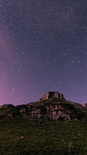 A dramatic mountain landscape under a twilight sky filled with swirling stars.