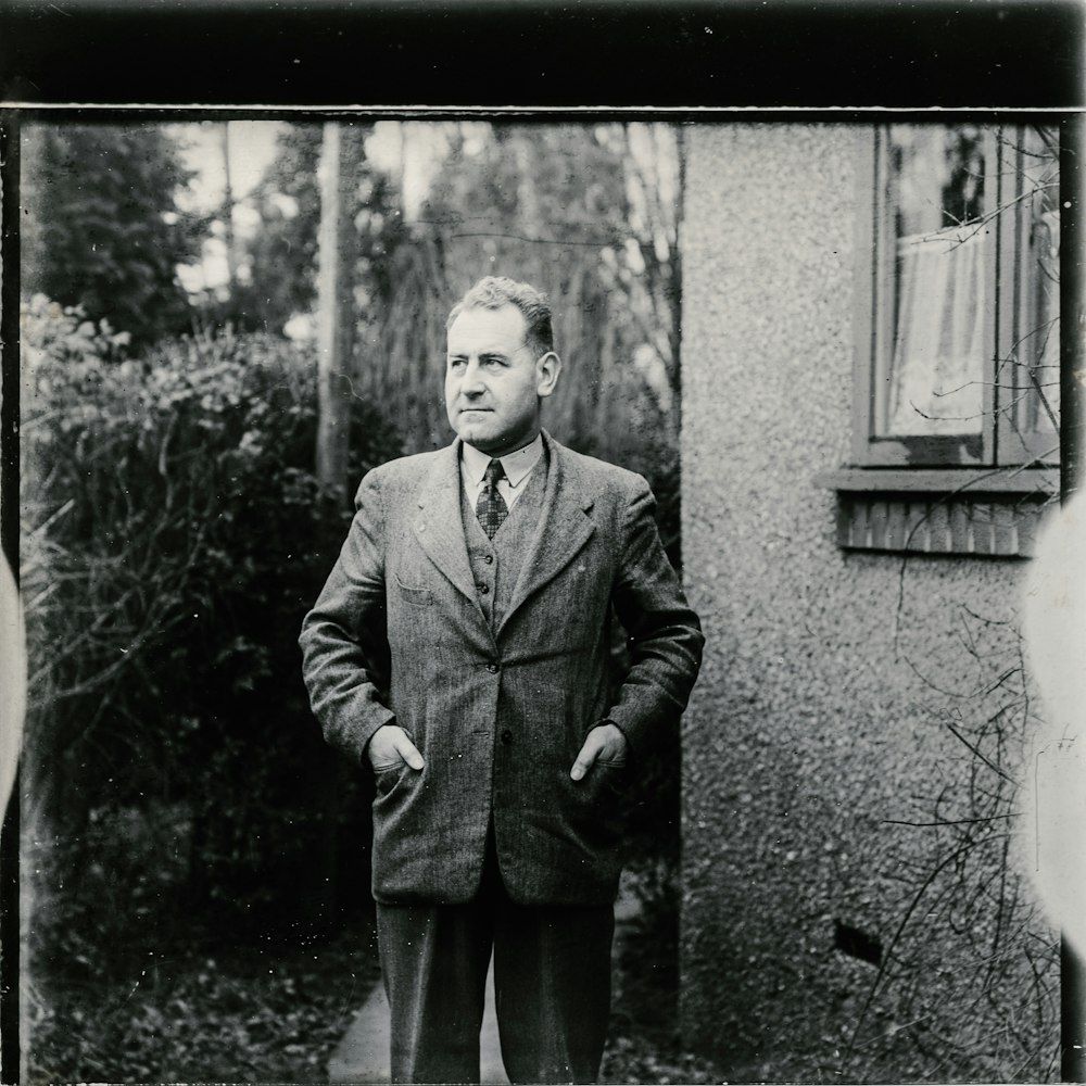 Foto en escala de grises de hombre con traje de pie junto a la pared con espejo