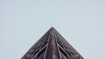 A low-angle shot of a tall building against a clear sky, showcasing sharp lines and a minimalist aesthetic. The structure's facade is marked by repetitive windows and a muted color palette.