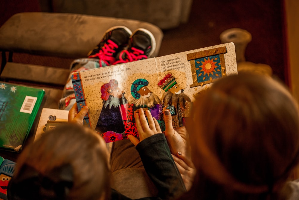 two childrens reading book while sitting on brown sofa