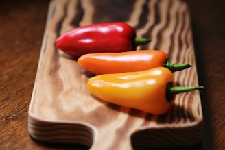 A vibrant assortment of red, yellow, and orange bell peppers on a wooden cutting board.