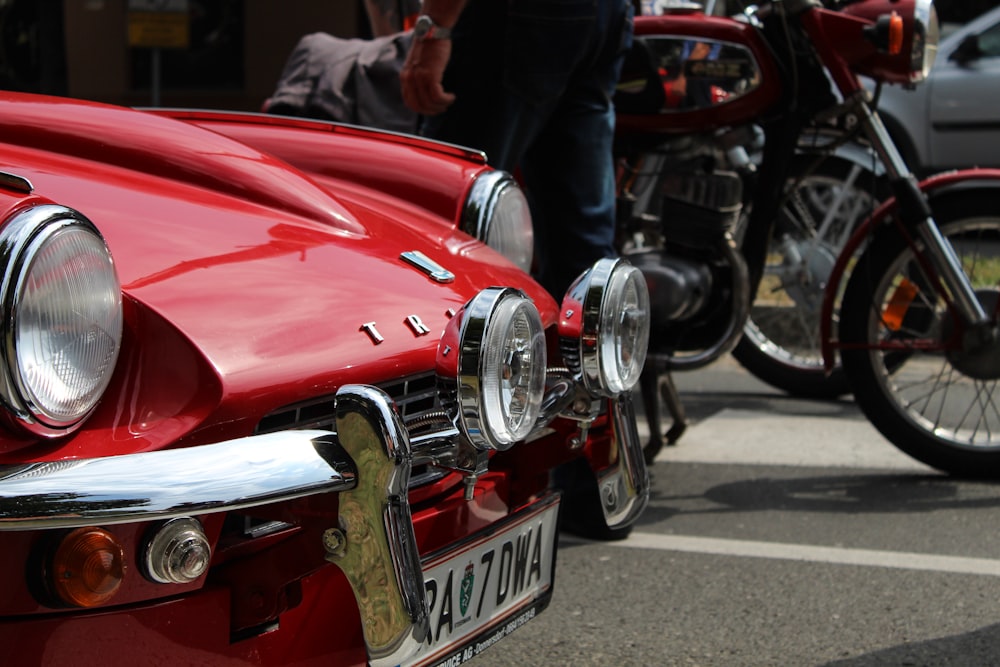 vintage red car near person driving motorcycle during daytime