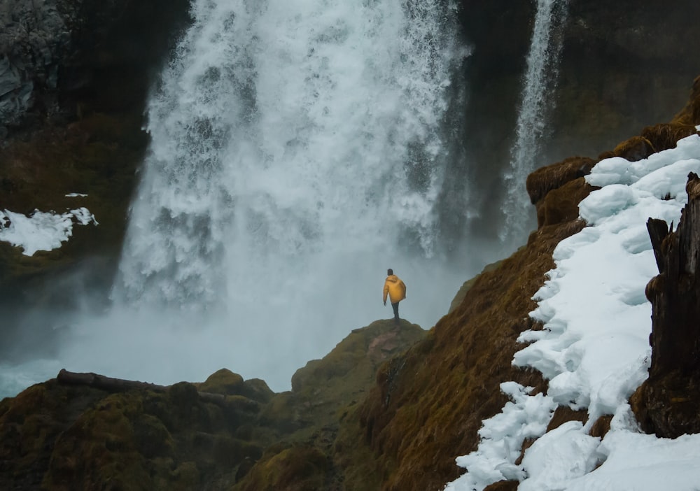 person hiking on brown mountain near waterfalls