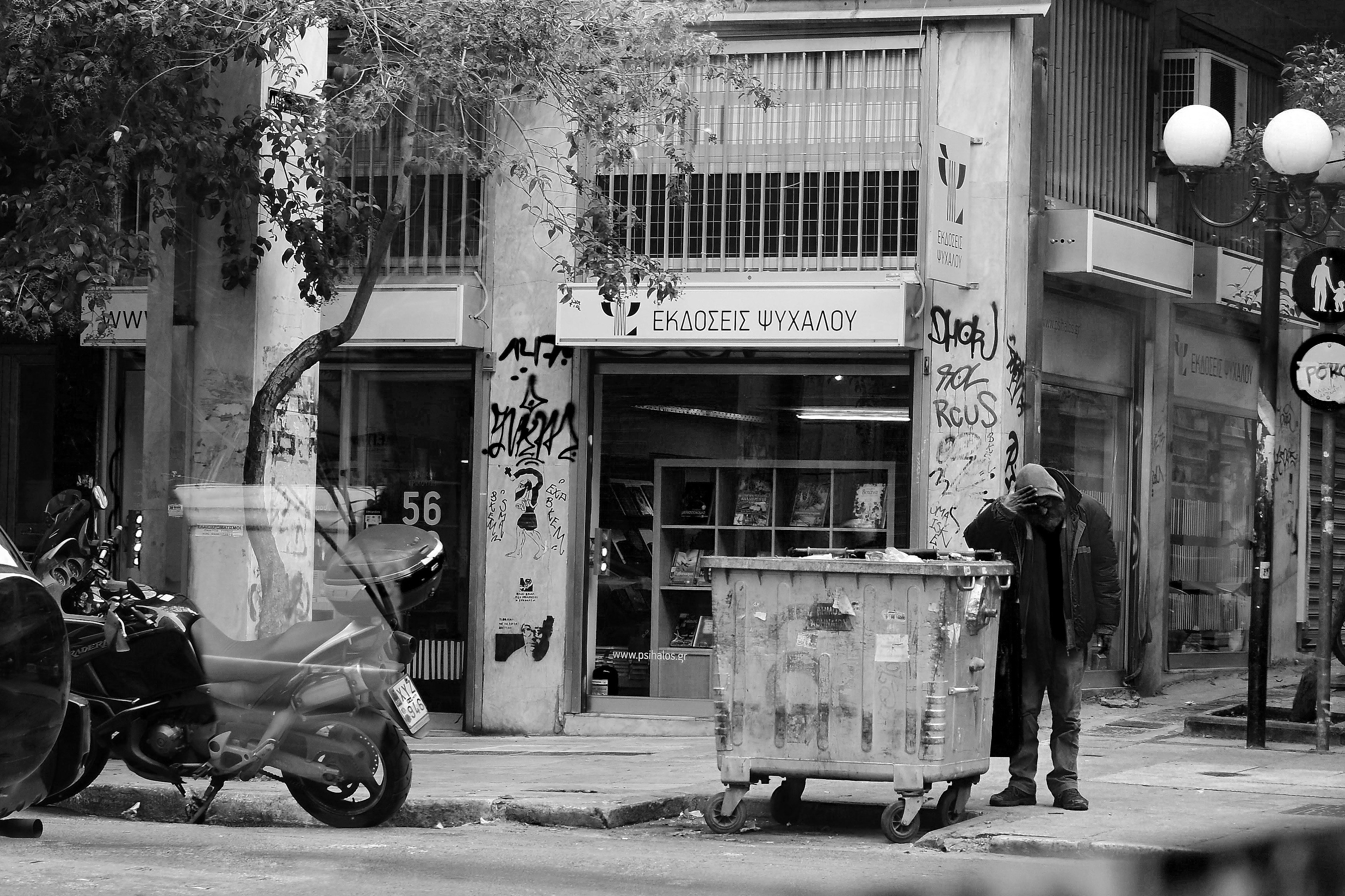 grayscale photography of man standing beside trash can