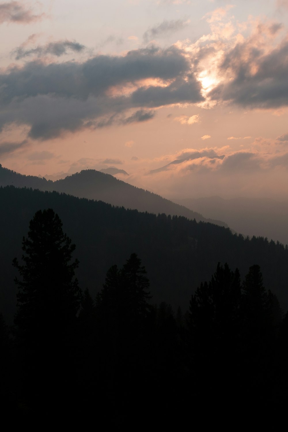 the sun is setting over the mountains and trees