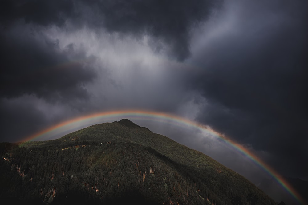 Foto ad angolo basso della montagna sotto l'arcobaleno e il cielo nuvoloso durante il giorno
