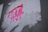 A partially torn and weathered sticker with the word 'ART' prominently visible in bright pink and partially obscured white lettering, adhered to a textured, off-white surface.