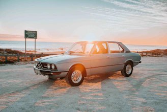 A gleaming vintage car parked on a winding coastal road at sunset, with the sea shimmering in the background.