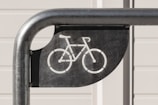 A metal bike rack with a bicycle symbol cut into a black metal plate, against a light-colored background with horizontal paneling.
