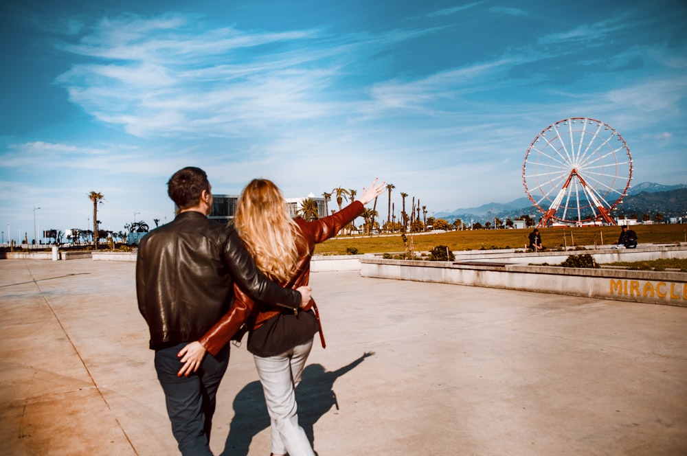 couple walking girl pointing red ferris wheel under blue sky and white clouds