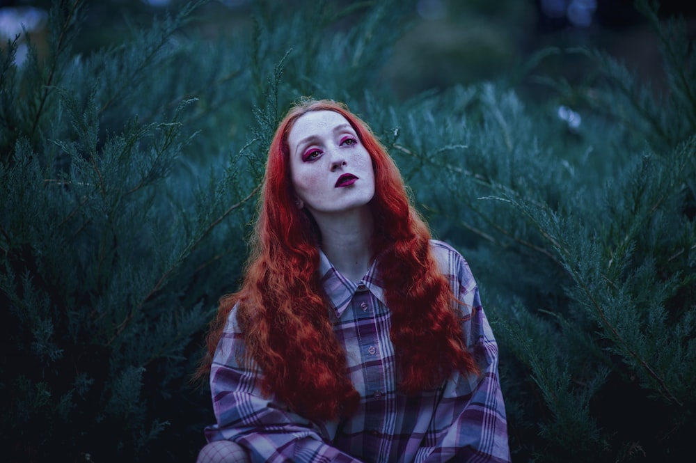 mulher com cabelo vermelho e batom vermelho perto de plantas de folhas verdes