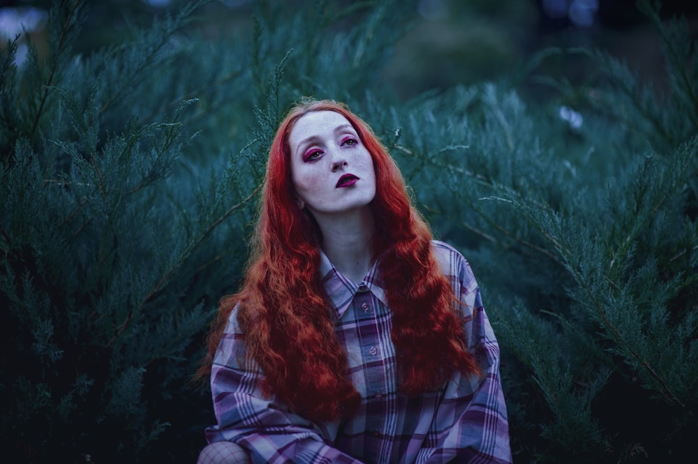 femme aux cheveux roux et rouge à lèvres rouge près des plantes à feuilles vertes