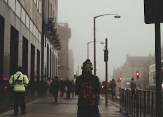 person wear black coat and backpack walking on sidewalk