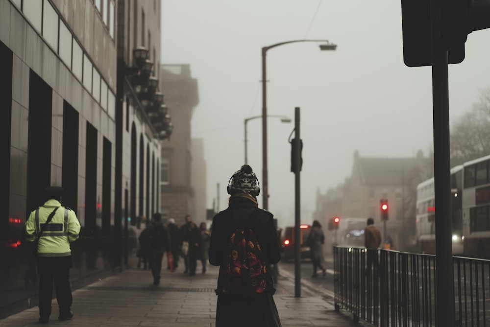 person wear black coat and backpack walking on sidewalk