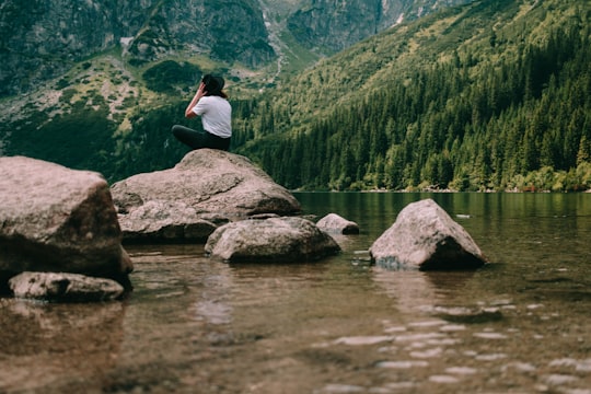 person sitting on rock formation facing mountains in Morskie Oko Poland