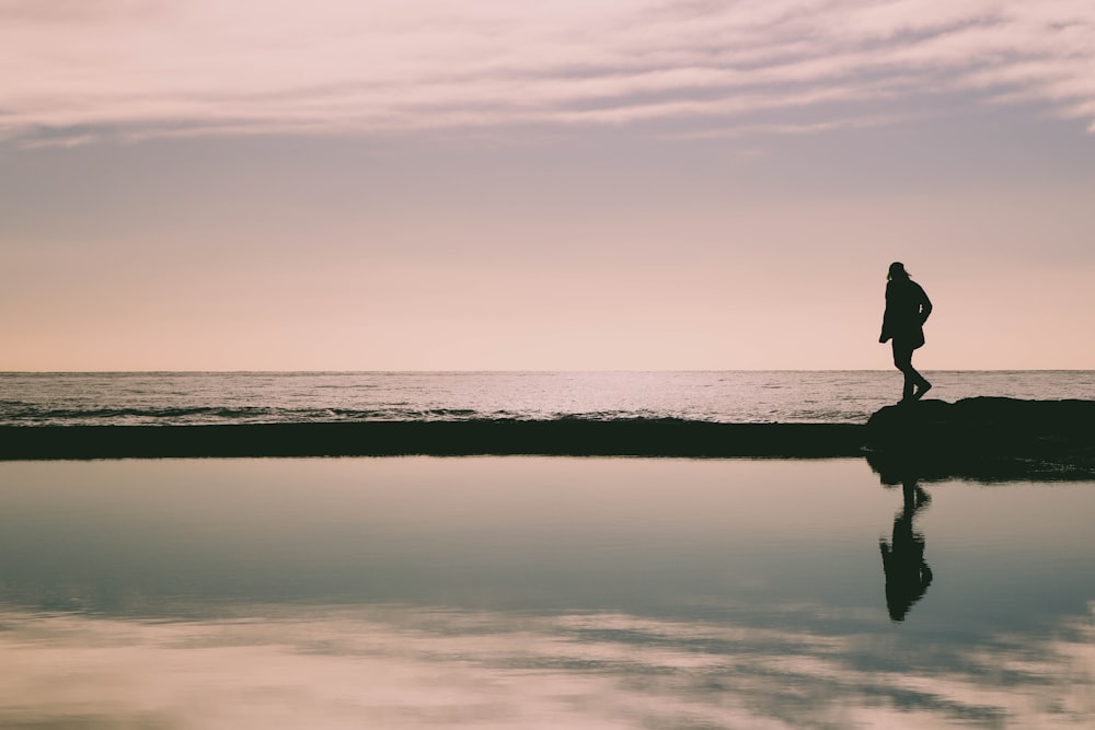 silhouette of woman on rock formation in seashore