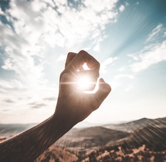 photography of sun glaring through the hole of finger