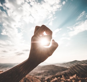 photography of sun glaring through the hole of finger