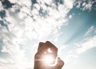 photography of sun glaring through the hole of finger