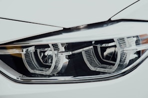 A close-up view of a sleek car headlight with a modern design. The headlight features intricate detailing and reflective surfaces, highlighting its precision engineering.
