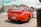 A bright red sports car is parked on the street at an intersection in a small town. The license plate indicates it is from Ontario. Surrounding the car are other vehicles, buildings with signage, and traffic lights. The scene has clear skies and a casual urban atmosphere.