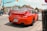 A bright red sports car is parked on the street at an intersection in a small town. The license plate indicates it is from Ontario. Surrounding the car are other vehicles, buildings with signage, and traffic lights. The scene has clear skies and a casual urban atmosphere.