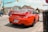A bright red sports car is parked on the street at an intersection in a small town. The license plate indicates it is from Ontario. Surrounding the car are other vehicles, buildings with signage, and traffic lights. The scene has clear skies and a casual urban atmosphere.