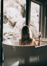 woman in white bathtub holding clear drinking glass