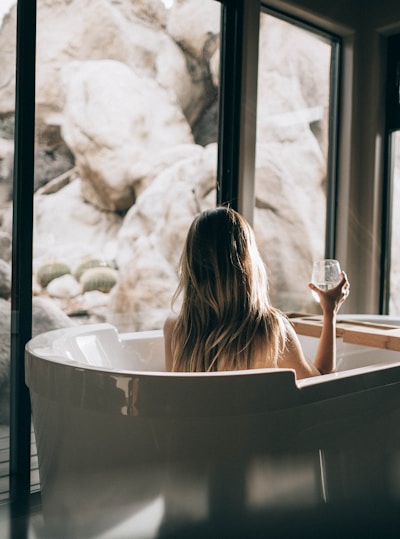 woman in white bathtub holding clear drinking glass