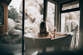 woman in white bathtub holding clear drinking glass