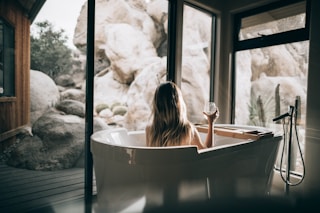 woman in white bathtub holding clear drinking glass