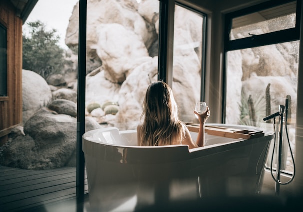 woman in white bathtub holding clear drinking glass