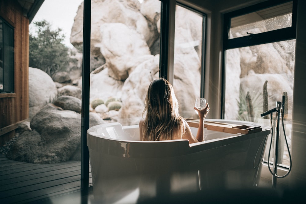 femme dans une baignoire blanche tenant un verre à boire transparent