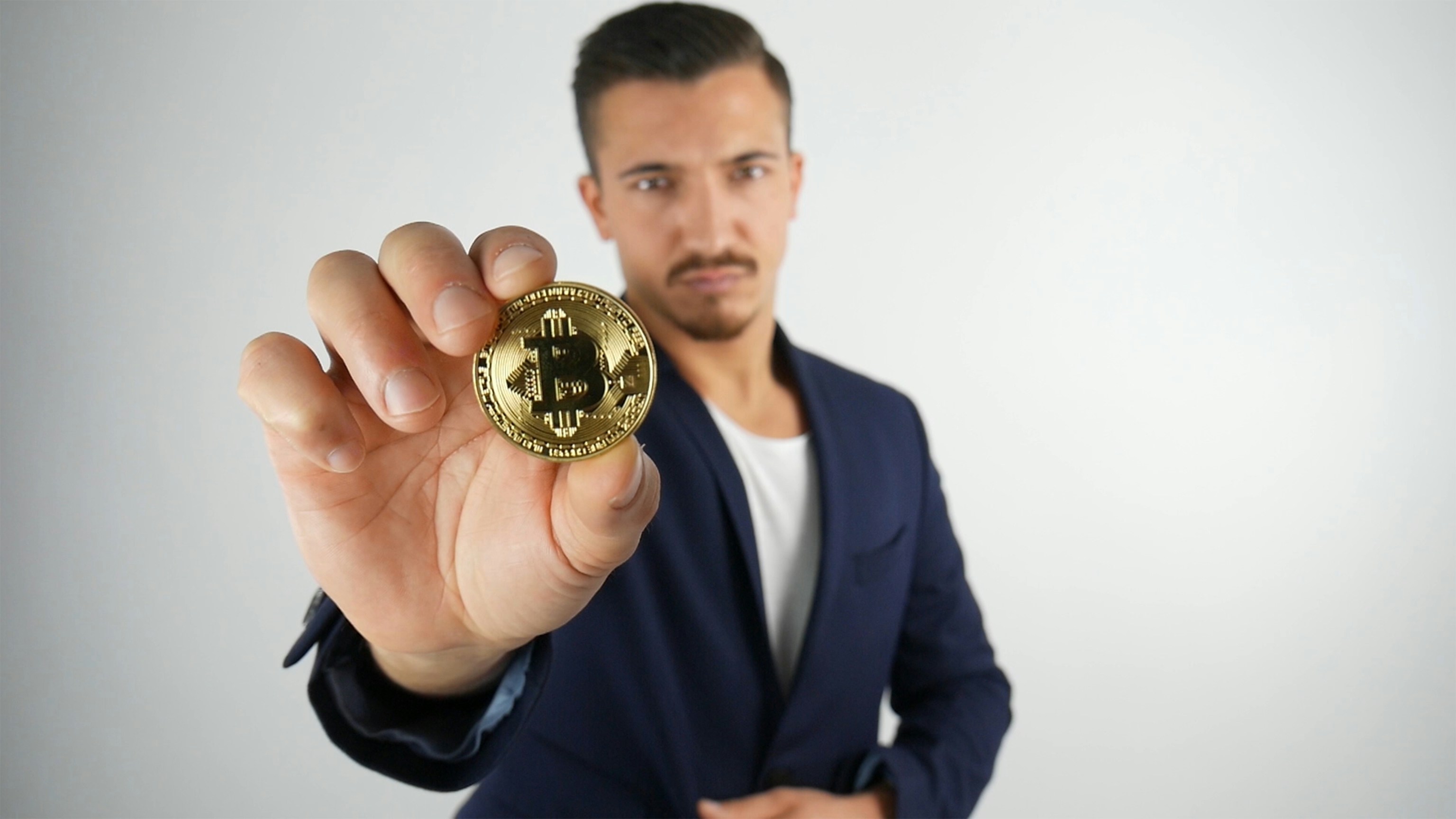 man in dark-blue suit jacket holding gold-colored coin