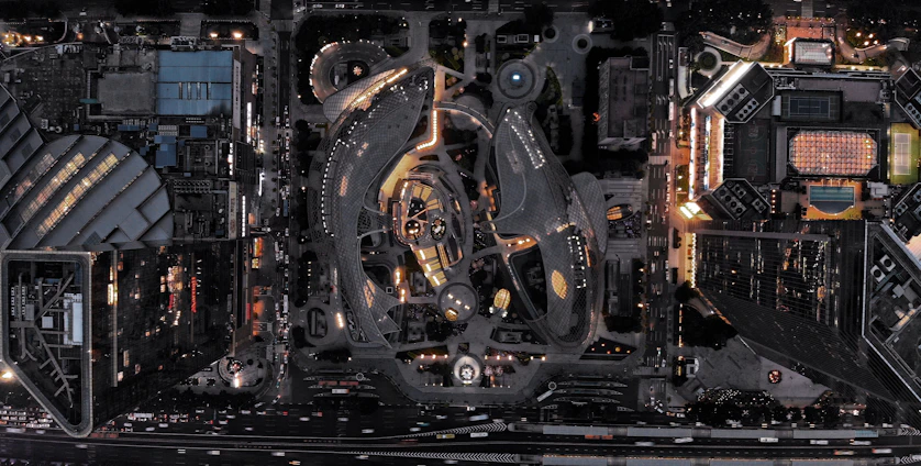 A nighttime aerial view of a modern architectural project in East London, illuminated subtly against a deep charcoal sky with gold accent lighting.