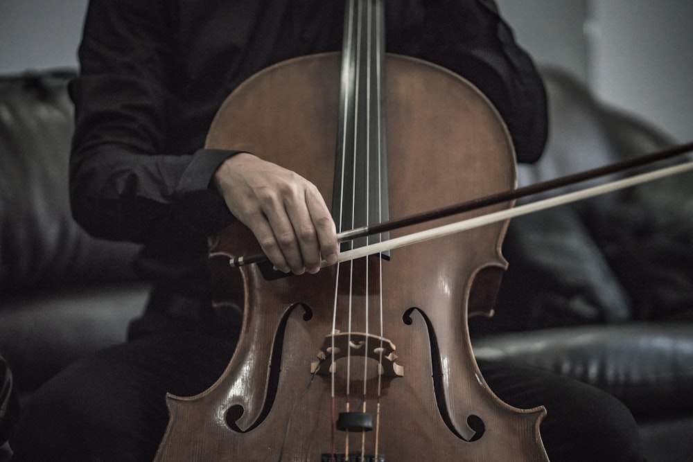 pessoa vestindo camisa social preta tocando instrumento de corda de violoncelo marrom