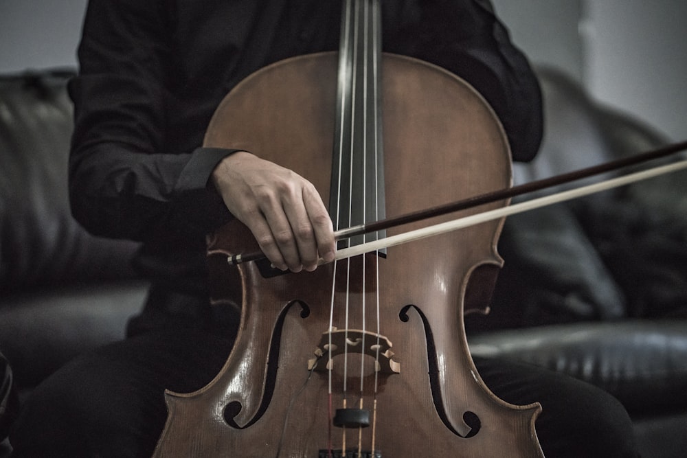 personne portant une chemise noire jouant d’un instrument à cordes de violoncelle marron