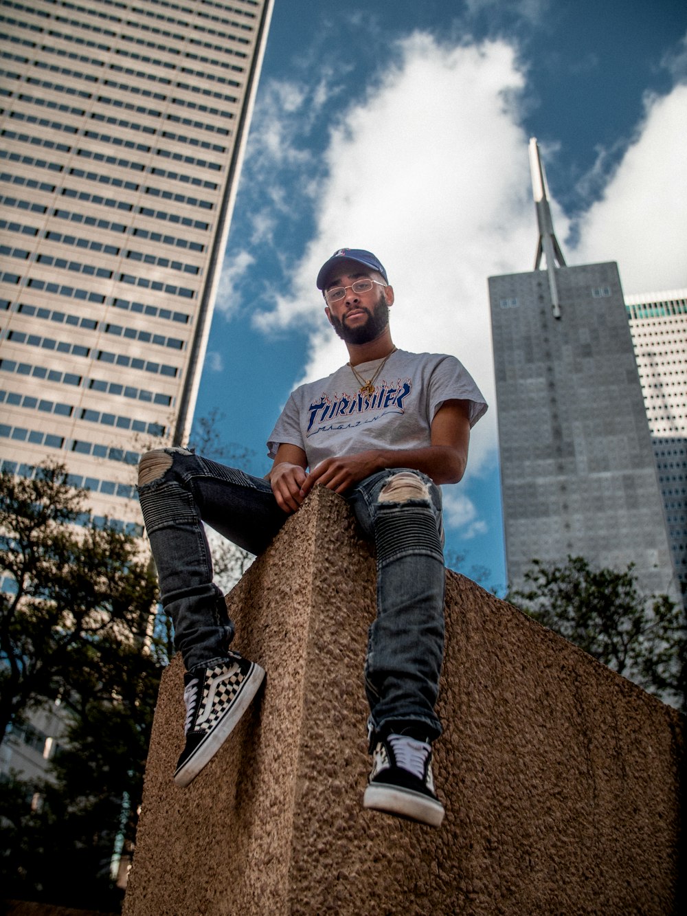 homem de top branco e jeans azul angustiado sentado em rocha de concreto marrom