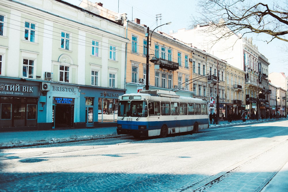 white and blue vehicle passing by white and orange concrete buildings during daytime