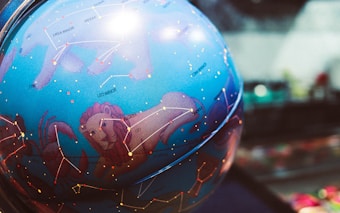 A blue celestial globe depicting various constellations, including detailed illustrations and labels such as Leo, Ursa Major, and Leo Minor. The globe features intricate lines connecting stars within the constellations against a vibrant blue background.
