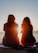 two woman sitting on beach sand while facing sunlight