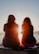two woman sitting on beach sand while facing sunlight