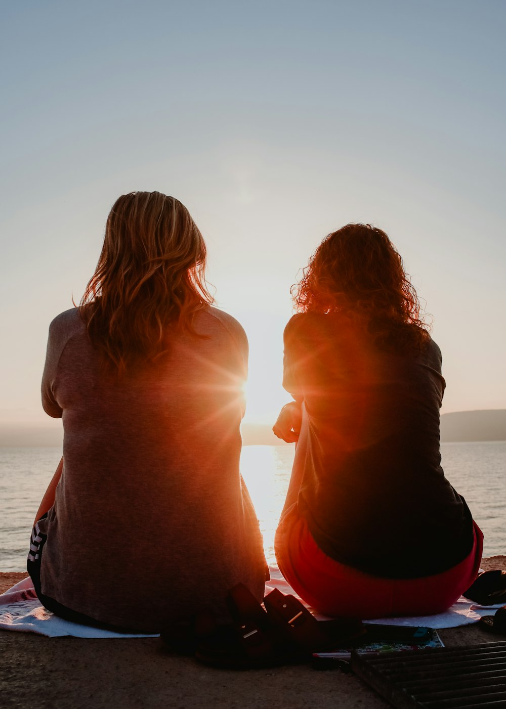 two woman sitting on beach sand while facing sunlight