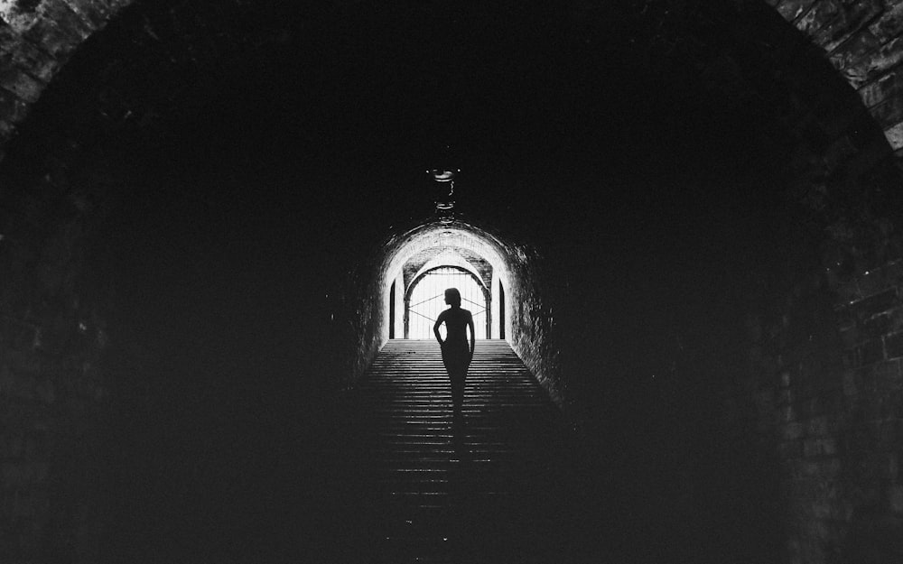 a person walking down a dark tunnel with a light at the end