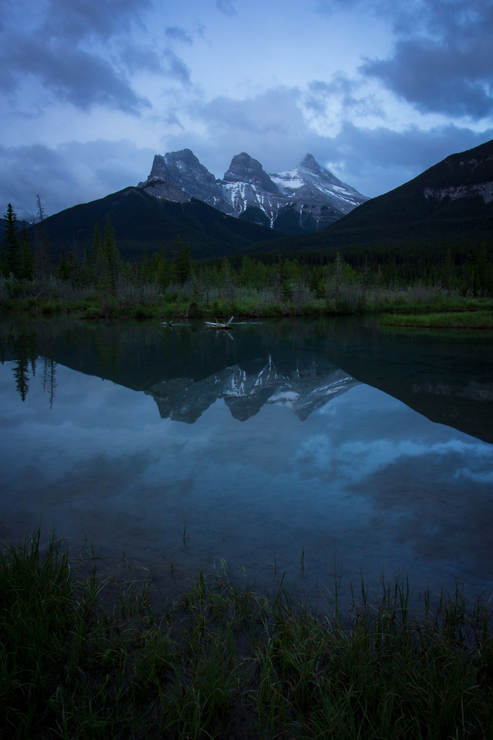 body of water near rocky mountain under gray sky