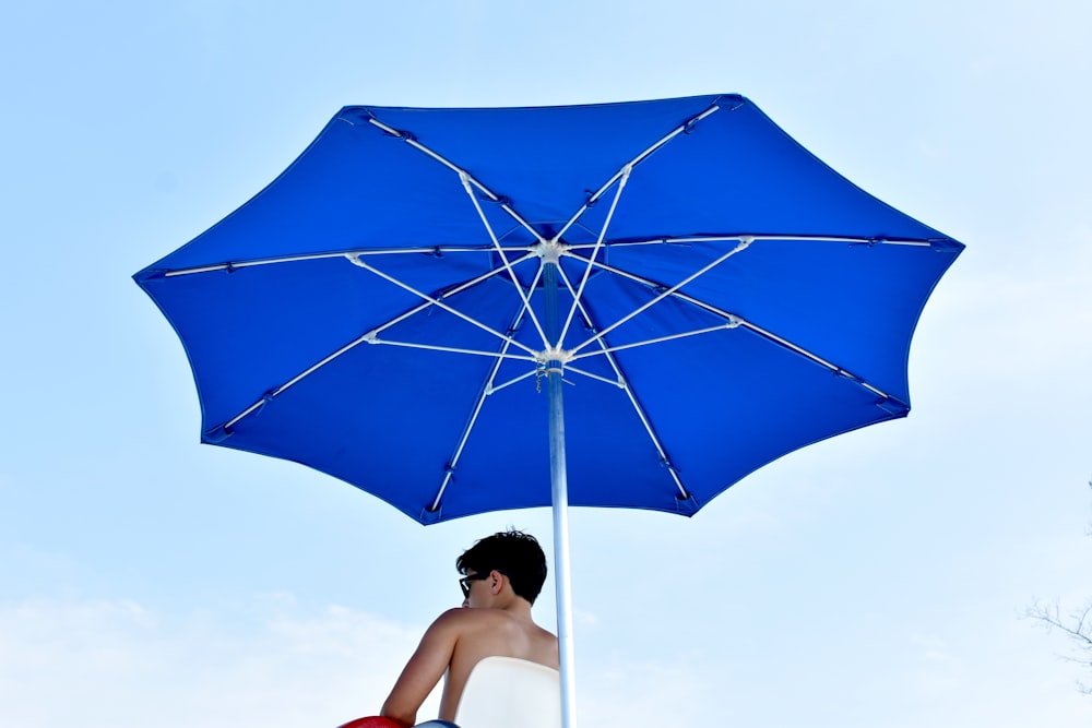 Mann sitzt auf Stuhl unter blauem Sonnenschirm