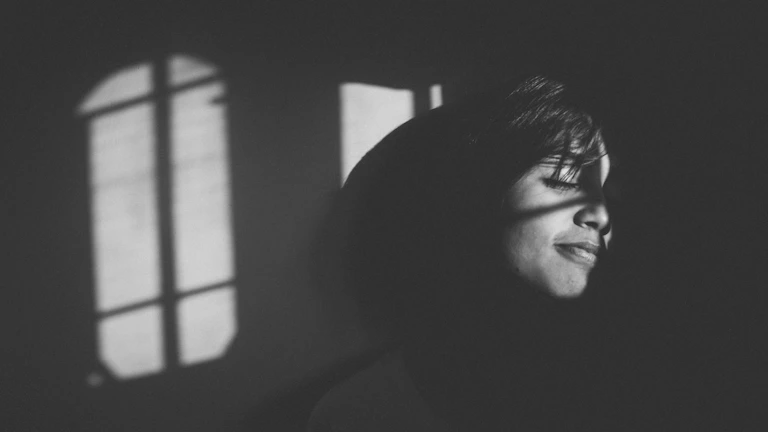 A black and white portrait of a grandmother smiling warmly, framed by soft natural window light