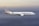 A large commercial airplane with the American logo is flying through an open sky with soft gradient hues ranging from light blue to gray.